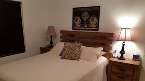 A bedroom with a bed, two nightstands, a lamp, a wall-mounted picture, and a window with blinds. - Cozy stand alone cottage with Bermuda Character  (St.George's, Bermuda)