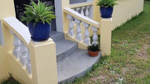 A yellow building with a white staircase and two potted plants on the steps. - Cozy stand alone cottage with Bermuda Character  (St.George's, Bermuda)