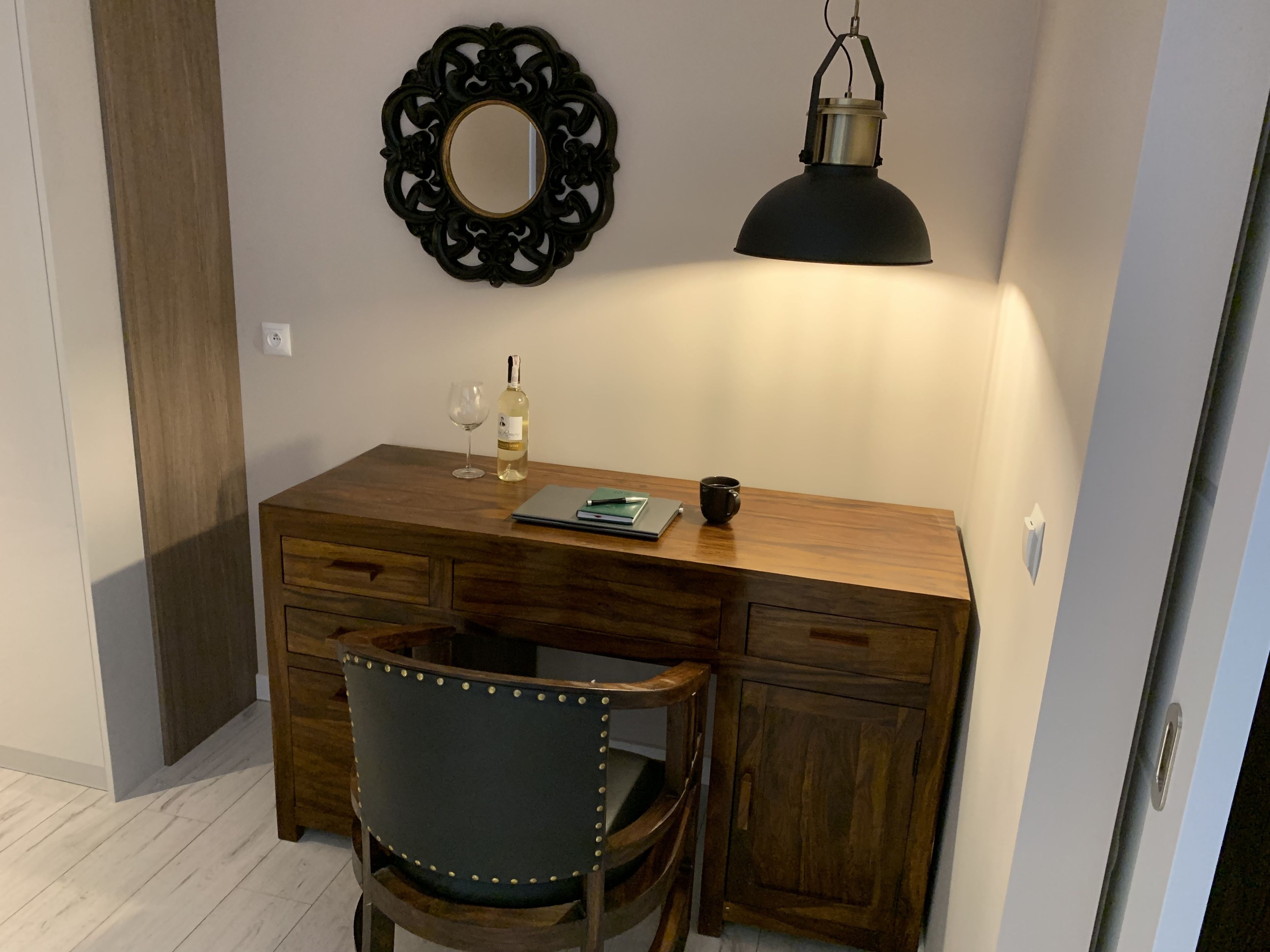 A wooden desk with a mirror, a bottle of wine, a glass, and a notebook.