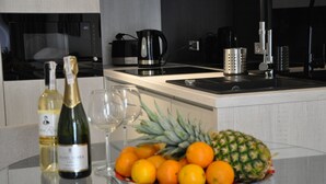 A modern kitchen with a glass-top island, a coffee maker, a kettle, and a fruit bowl with oranges and a pineapple. - ApartamentSun White (Wroclaw)