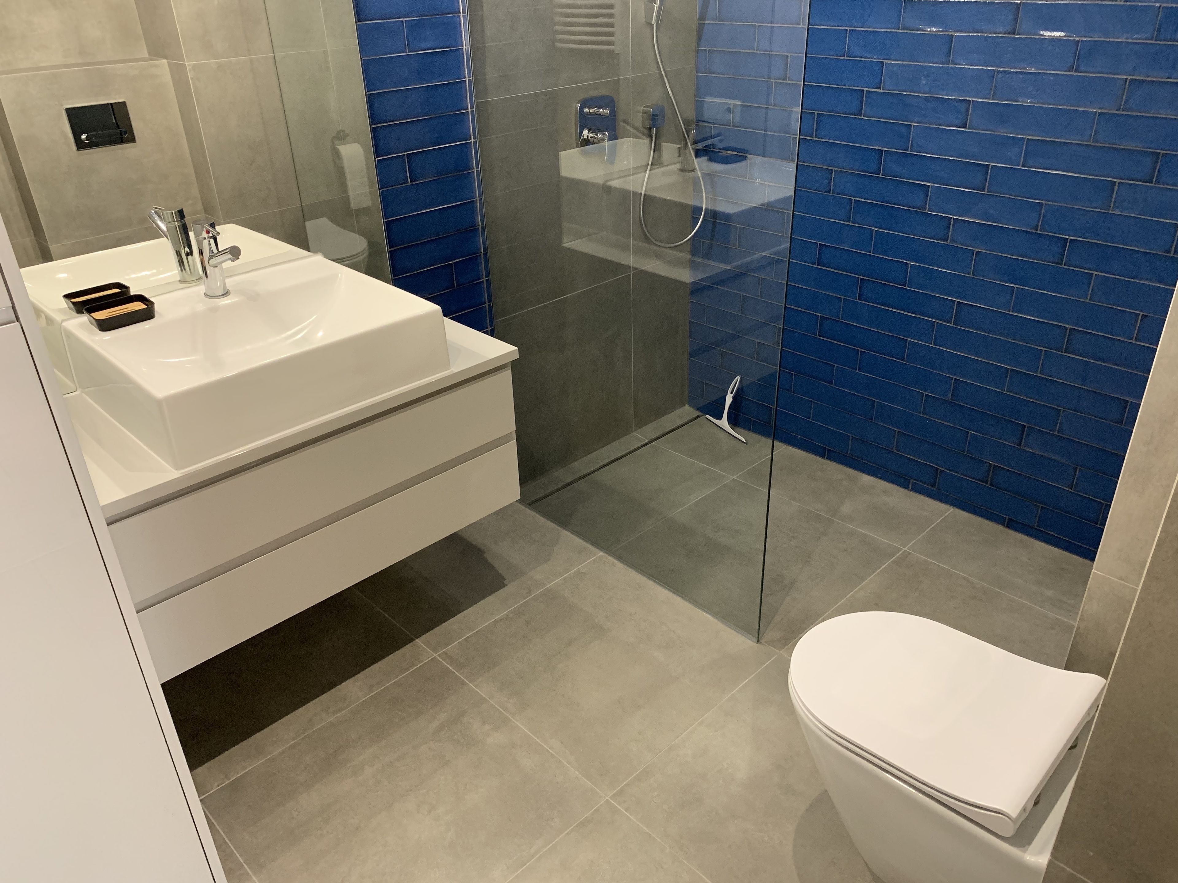 Un baño moderno con lavamanos blanco, espejo y cabina de ducha con paredes de vidrio.