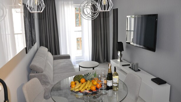 A modern living room with a sofa, a glass coffee table with fruits and drinks, a TV, and a wine bottle. - ApartamentSun White (Wroclaw)