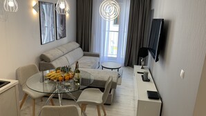 A modern living room with a glass dining table, a sofa, and a TV mounted on the wall. - ApartamentSun White (Wroclaw)
