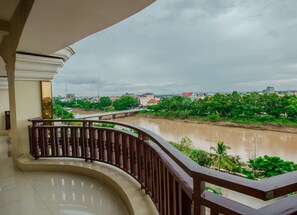 Un balcon donnant sur une rivière, avec une vue sur la verdure et des bâtiments éloignés.