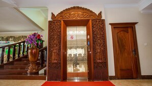 A wooden door with intricate carvings, a red carpet, and a staircase with a floral arrangement. - VY CHHE Hotel (Battambang)