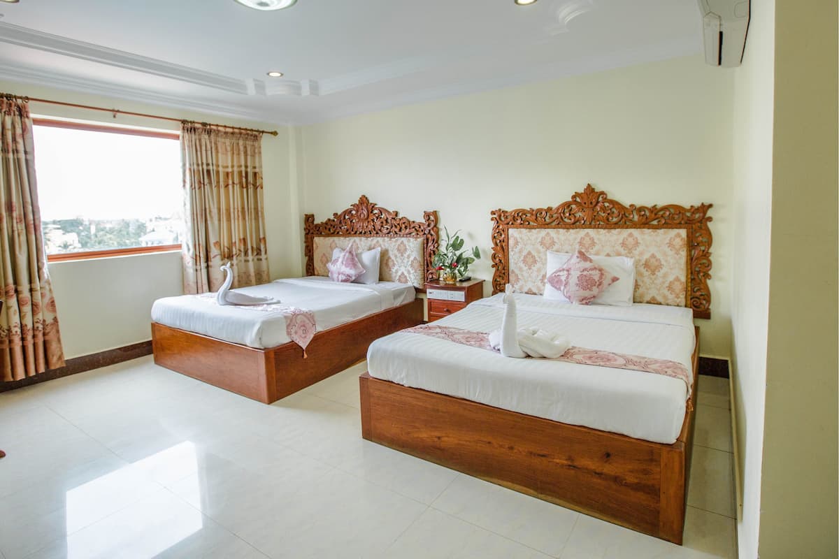 Une chambre d’hôtel avec deux lits en bois, une grande fenêtre avec des rideaux et un plafond doté d’un éclairage encastré.