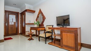 A room with a wooden desk, a television, a chair, a mirror, and a door with a red doormat. - VY CHHE Hotel (Battambang)