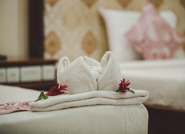 Une serviette blanche, soigneusement pliée et ornée de fleurs rouges, est posée sur le lit d’une chambre d’hôtel.