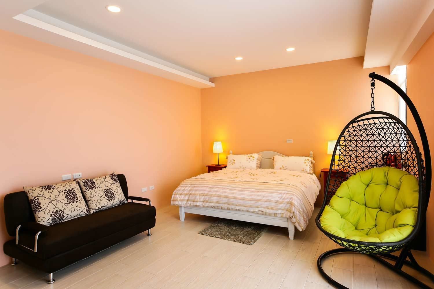 A bedroom with a bed, a hanging chair, and a sofa.