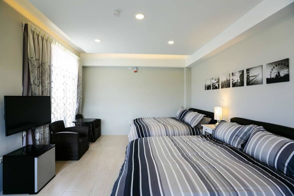 A hotel room with two beds, a TV, a small table, and a sofa.