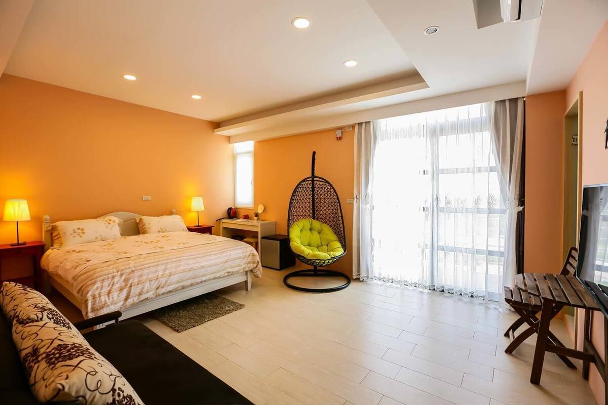 A hotel room with a bed, a hanging chair, a desk, a TV, and a view of the outside.