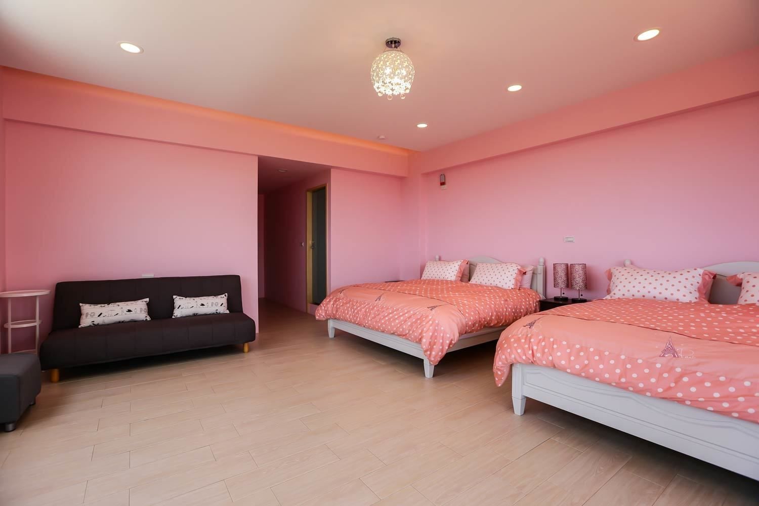 Une chambre avec des murs roses, deux lits avec une literie assortie, un canapé foncé et une petite table.