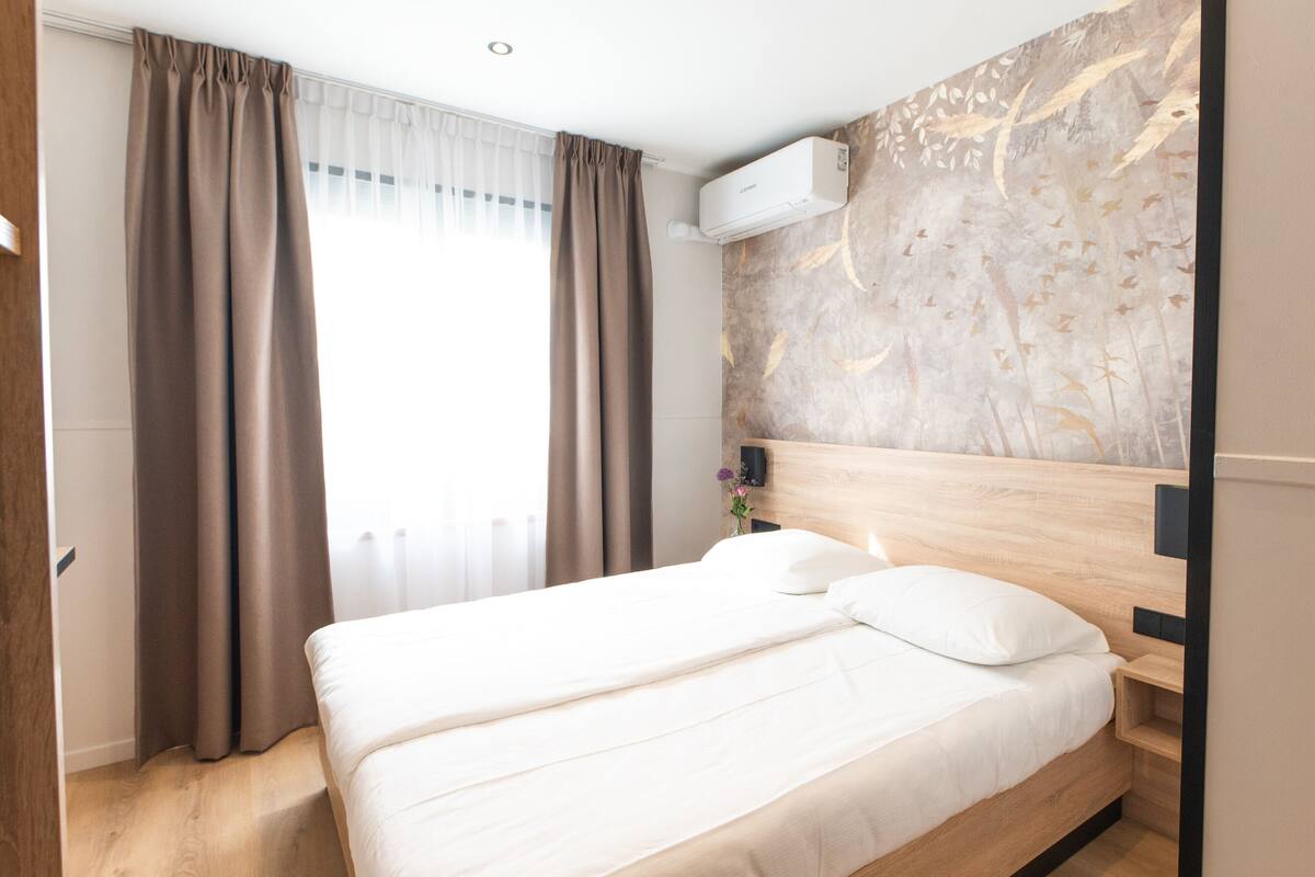 A modern hotel room with a large bed, wooden headboard, and a wall-mounted air conditioner.