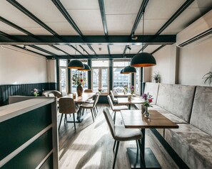 A modern restaurant interior with wooden tables and chairs, a bar area, and large windows offering a city view. - Hotel van Gelder (Amsterdam)