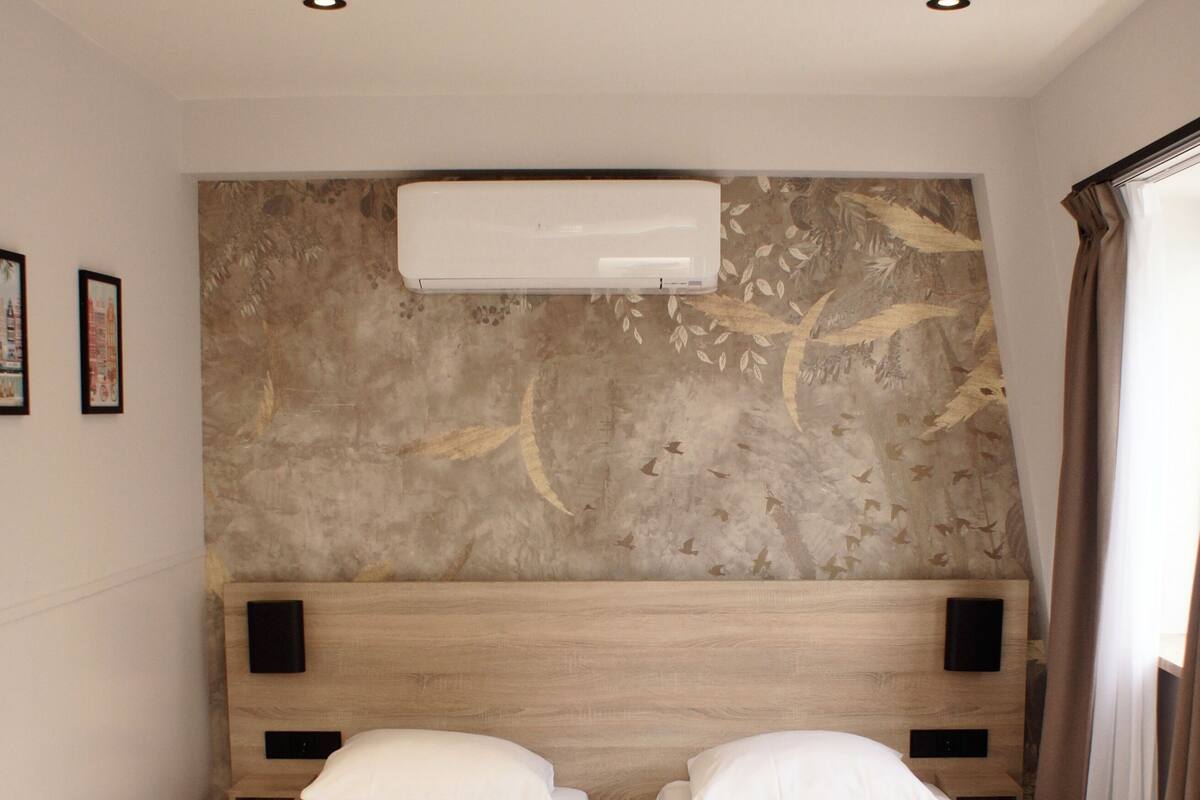 A room with two single beds, wooden headboards, a large air conditioning unit, and a stone-patterned wall.