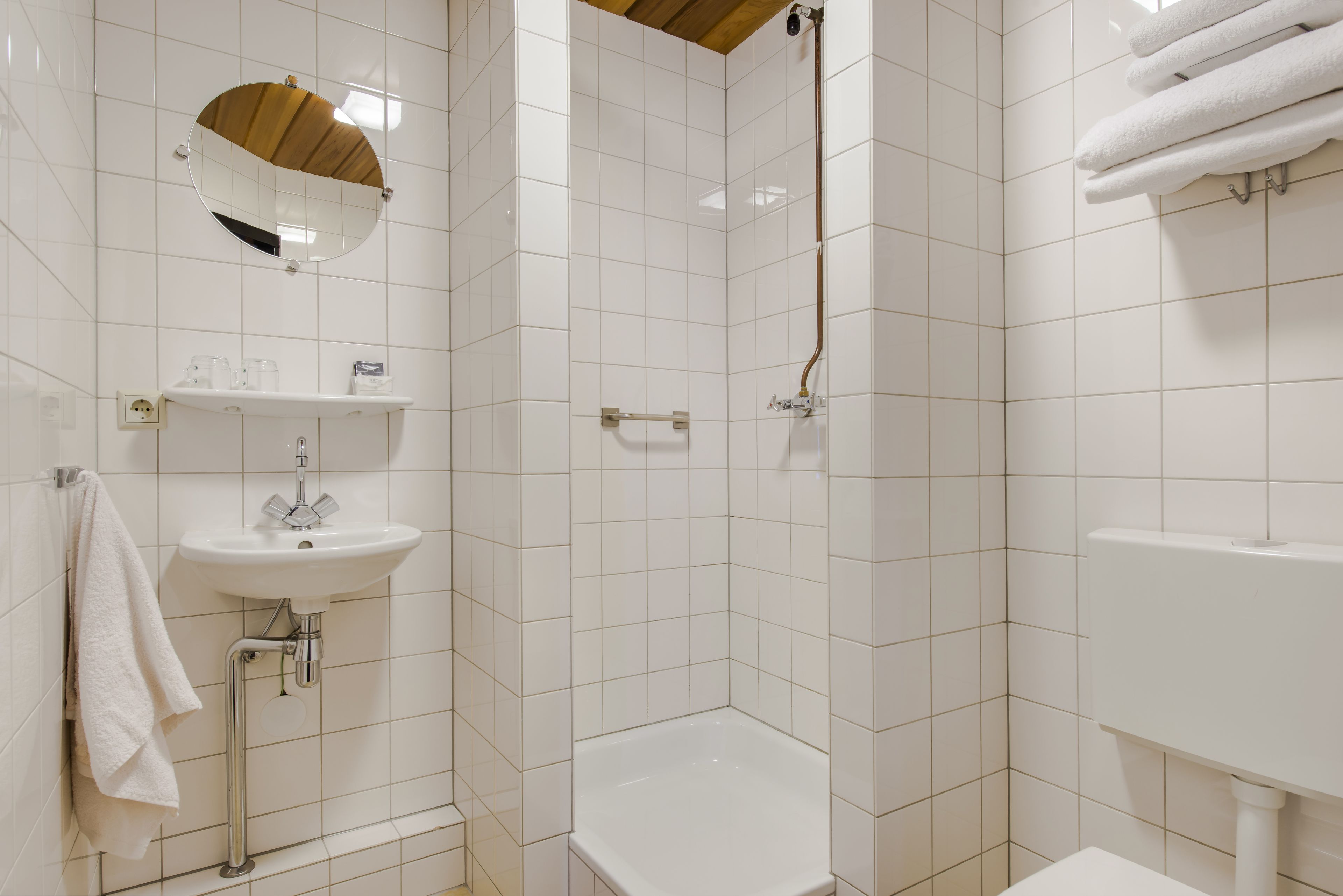 A modern bathroom with white tiles, a sink, a mirror, and a shower area.