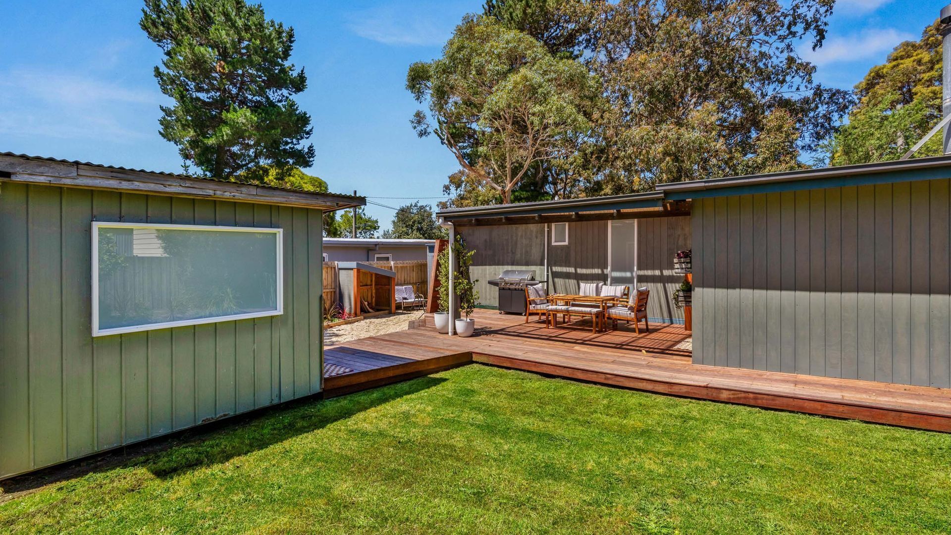 A backyard with a wooden deck, a barbecue grill, and a seating area with a table and chairs.