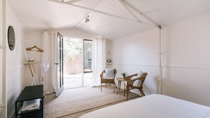 A bedroom with a bed, two wicker chairs, a small table, a fan, and a door leading to an outdoor area. - Dovestones by the Sea - Inverloch (Inverloch)