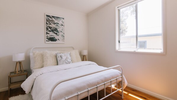 A bedroom with a bed, a bedside table, a lamp, a picture on the wall, and a window.