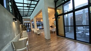 A spacious indoor area with wooden flooring, white wicker chairs, and large windows allowing natural light. - Good News Homestay (Hengchun)