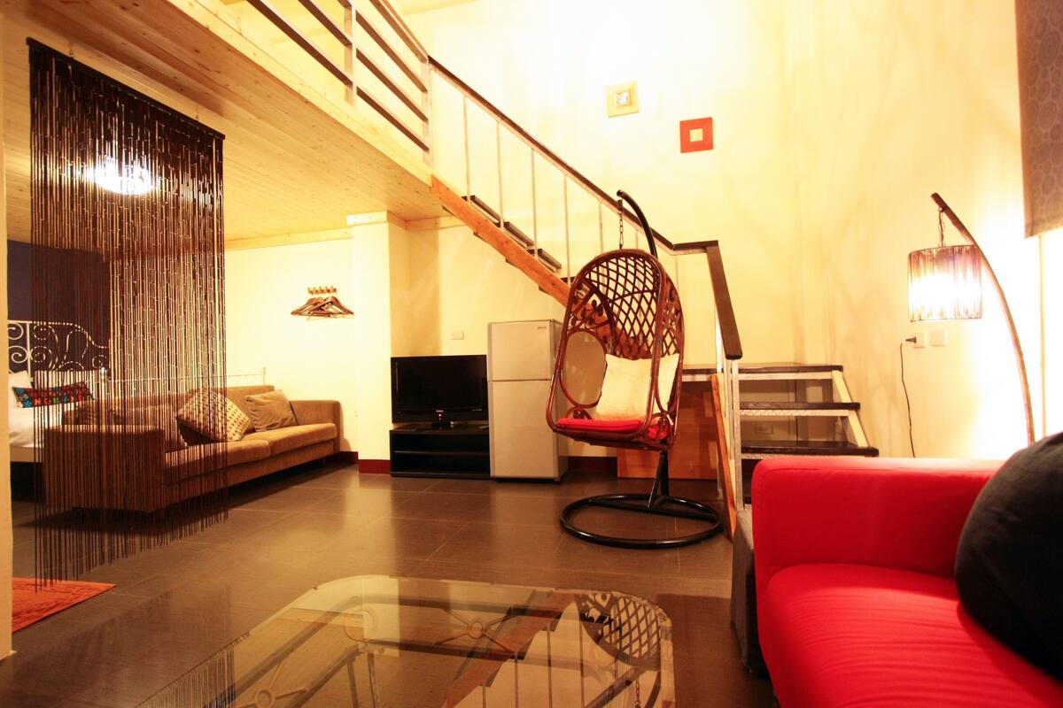 A living room with a sofa, a red chair, a glass coffee table, a TV, and a staircase.
