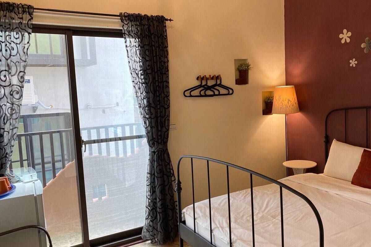 A bedroom with a bed, a nightstand, a lamp, and a view of the outside balcony.
