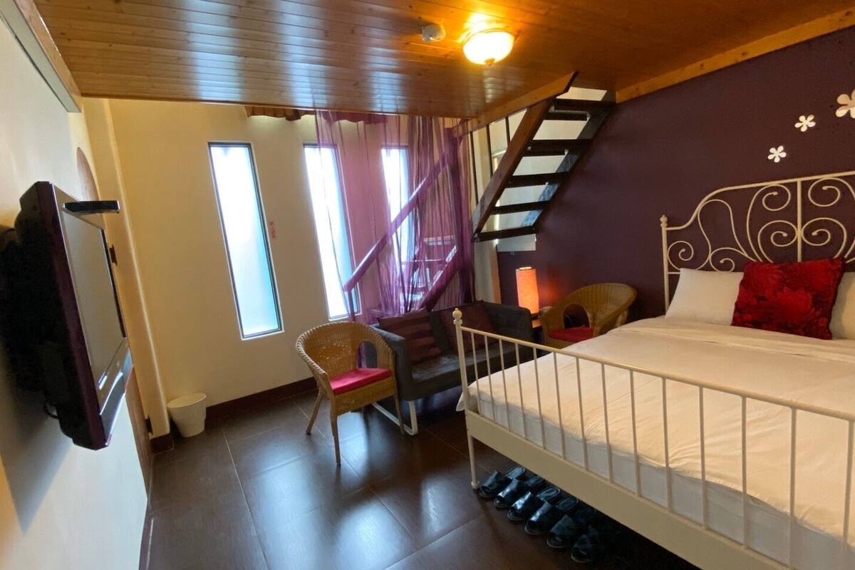A bedroom with a bed, a chair, a desk, a staircase, and a window.