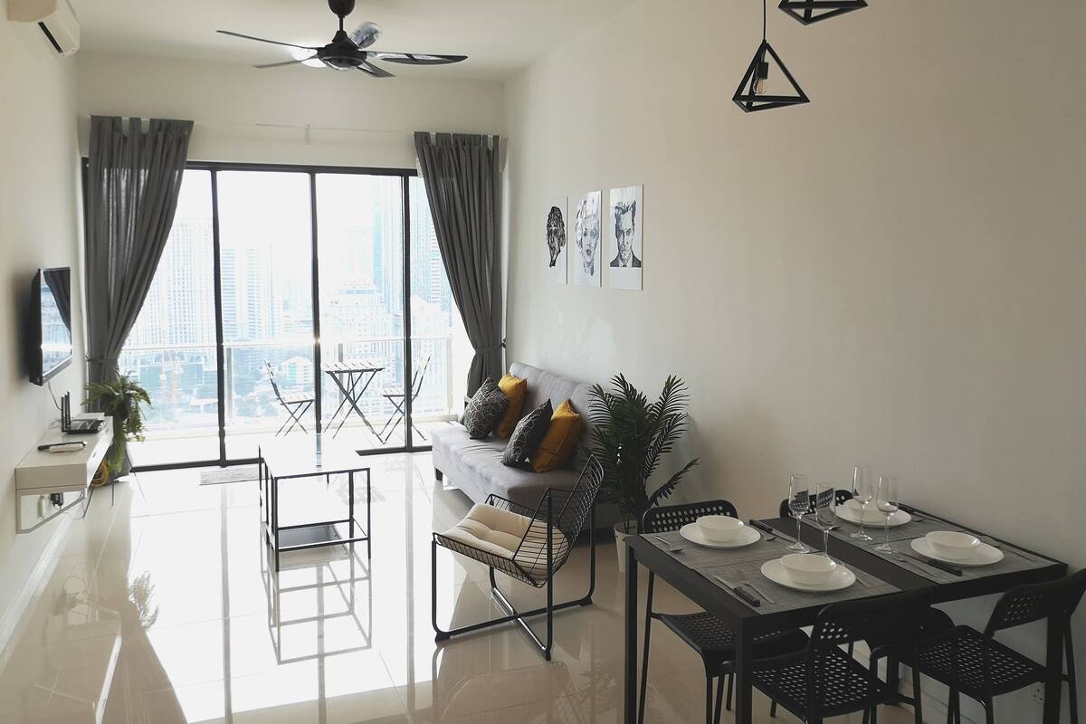 A modern living room with a dining area, large windows, a ceiling fan, and a city view.