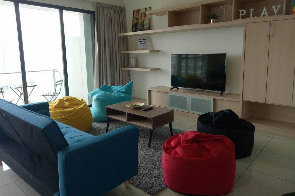 A modern living room with a sofa, bean bag, television, and a bookshelf.