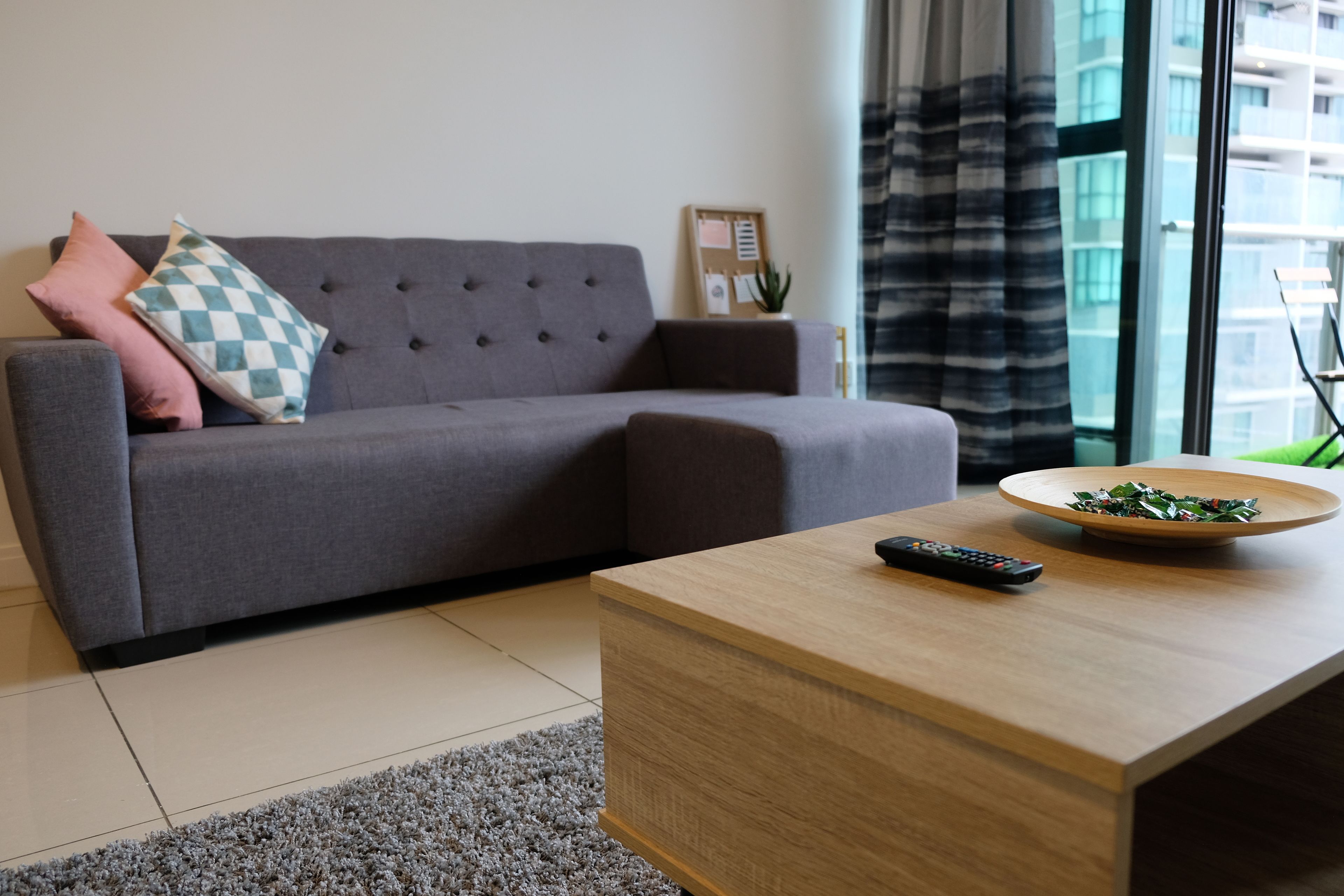 A modern living room with a grey sofa, a wooden coffee table, and a remote control.