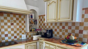 Une cuisine compacte avec un dosseret de carreaux, des meubles blancs et une machine à café.