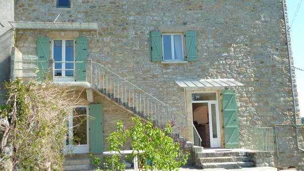 Un bâtiment en pierre avec un escalier menant à une porte, le tout entouré de verdure.