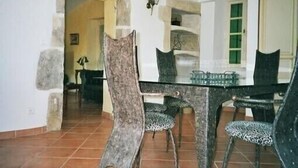 Un coin repas avec une table en verre et des chaises à motifs, des murs en pierre et une porte visible donnant sur une autre pièce.