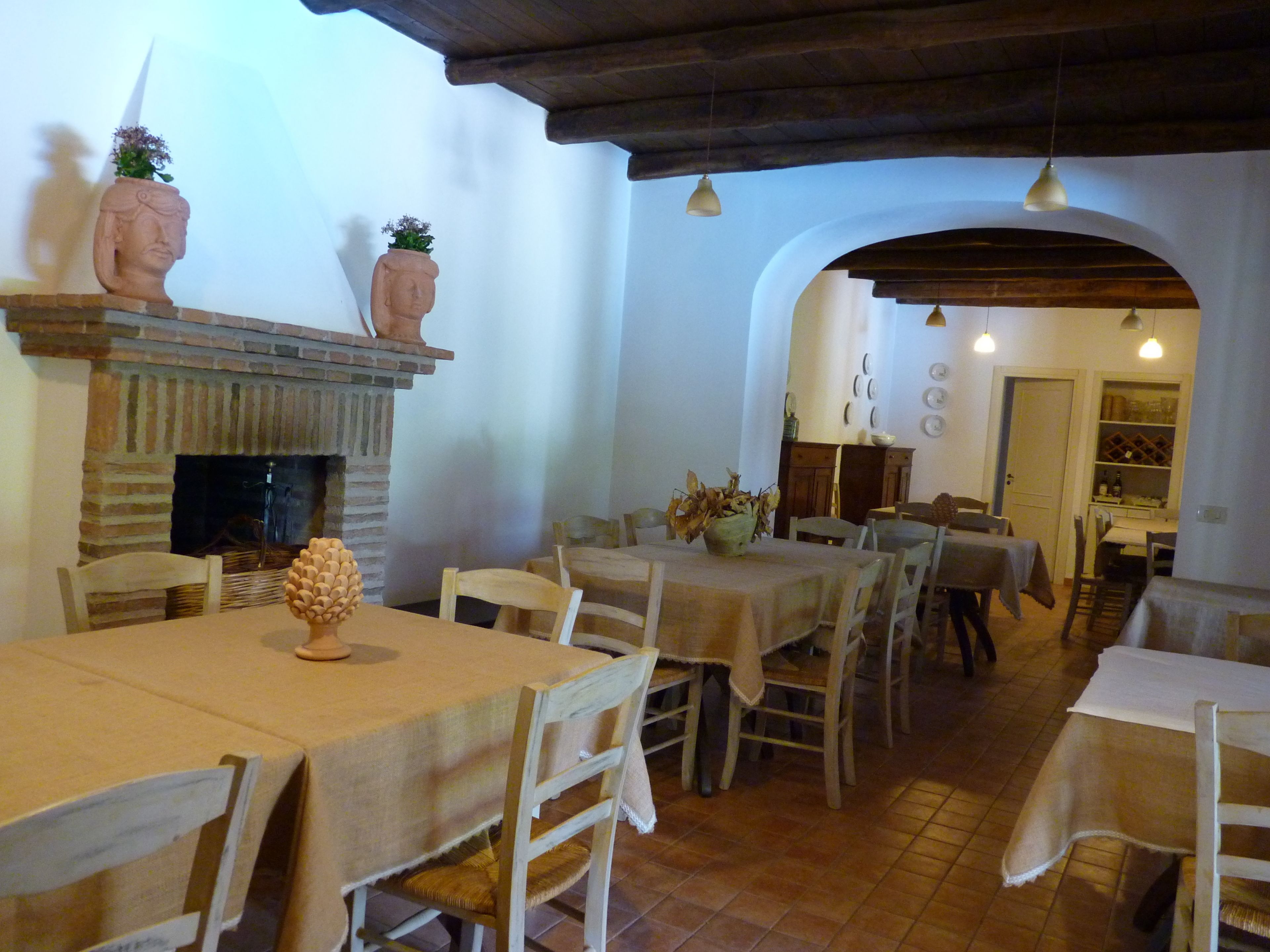 A dining area with multiple tables and chairs, a fireplace, and a kitchen area visible through an archway.