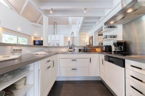 A modern kitchen with white cabinetry, a stainless steel range hood, and a built-in dishwasher.