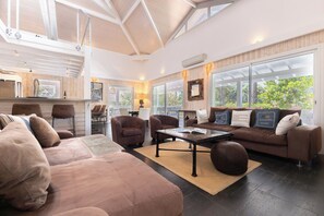 A spacious living area with a high ceiling, large windows, and a modern kitchen in the background.