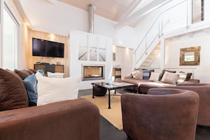 A spacious living room with a fireplace, a flat-screen TV, and a staircase.