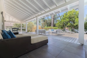 A covered outdoor living area with a sofa, chairs, and a dining table.