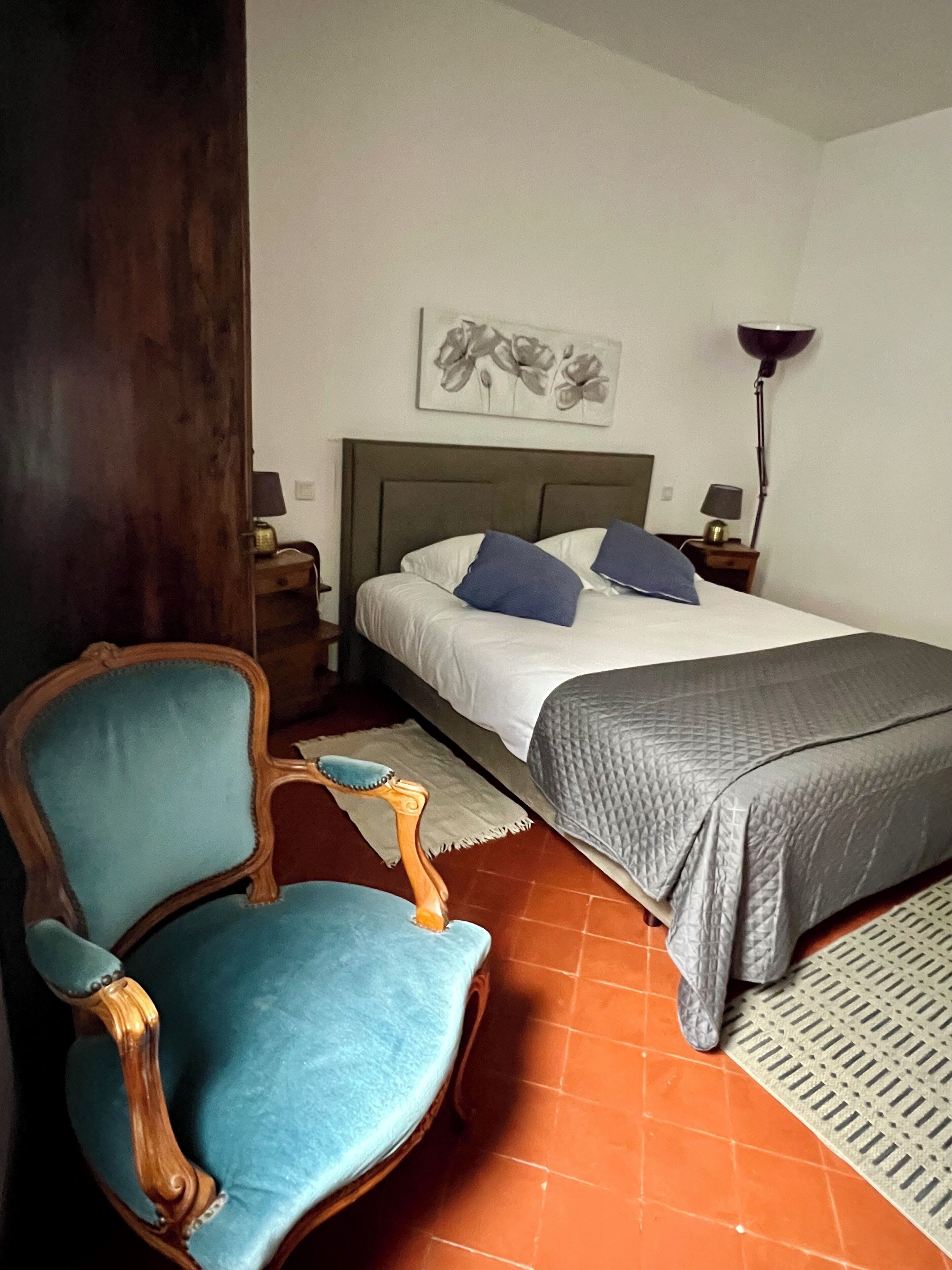 A bedroom with a bed, a chair, a nightstand, a lamp, and a wall art piece.