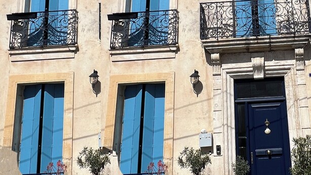 Un edificio con varios balcones, contraventanas azules y una puerta azul oscuro.