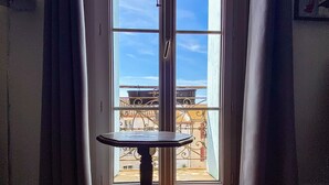 Habitación con una mesa frente a un amplio ventanal, suelo de baldosas y vistas a edificios.