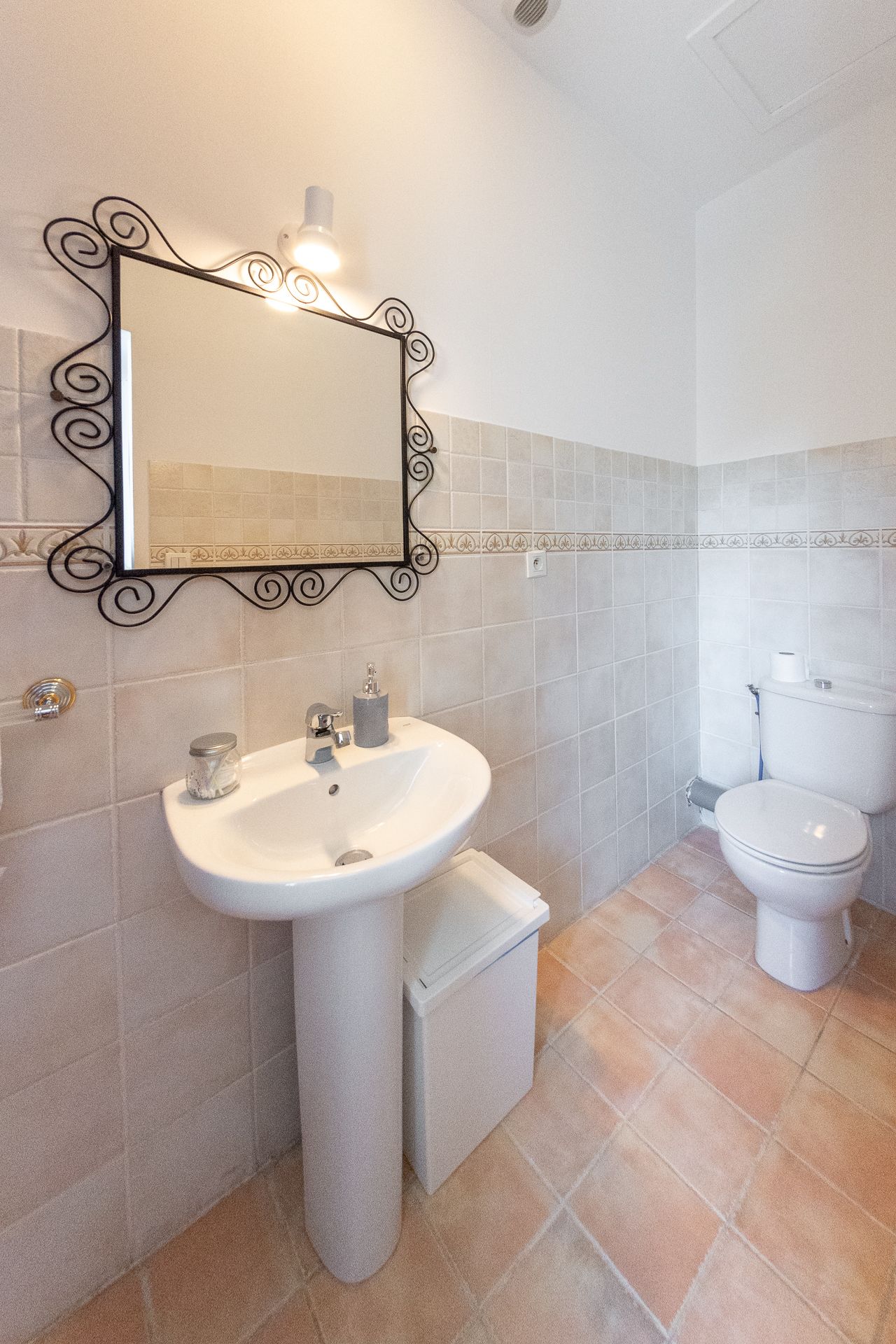 Een badkamer met een wastafel op voet, een toilet en een spiegel aan de muur met decoratieve lijst.