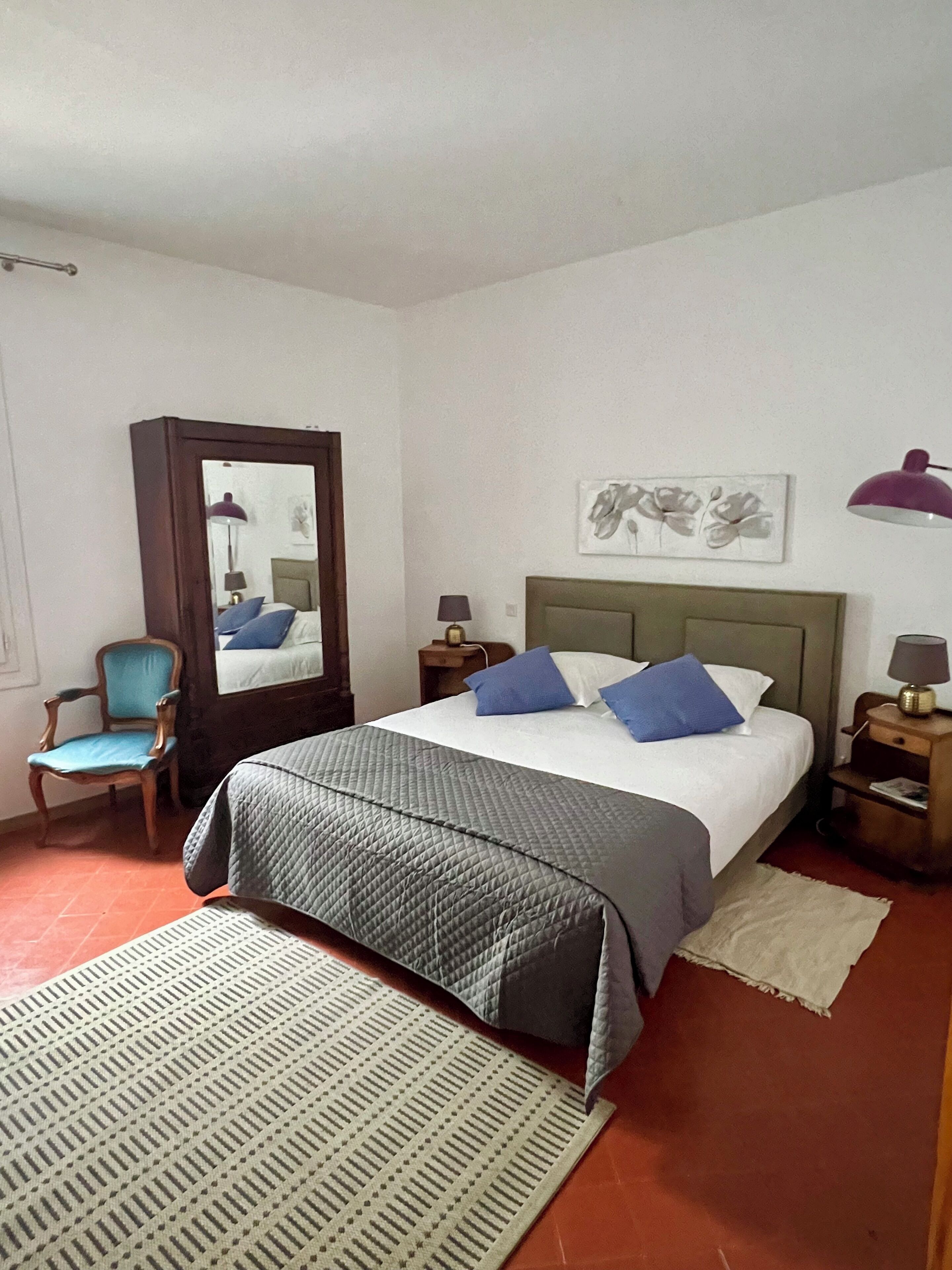 Een slaapkamer met een bed, een stoel, een spiegel, een nachtkastje en een lamp.