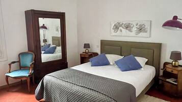 Een slaapkamer met een bed, een stoel, een spiegel, een nachtkastje en een lamp.