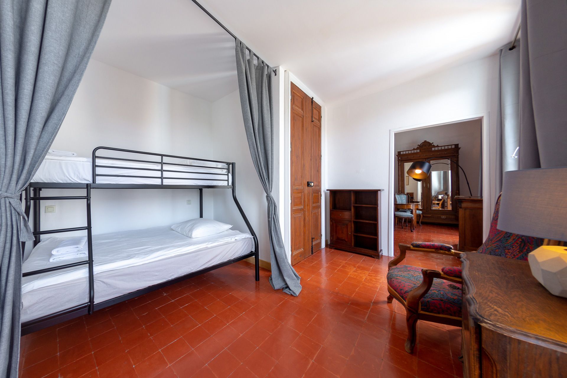 Une pièce avec un lit superposé, une porte en bois, un miroir, une chaise et une table.