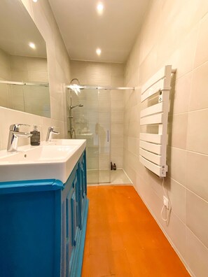 A modern bathroom with a glass shower enclosure, a white sink with a blue accent, and a white towel rack. - Entre MIDI - Maison d'Hôtes - B&B (Capestang)