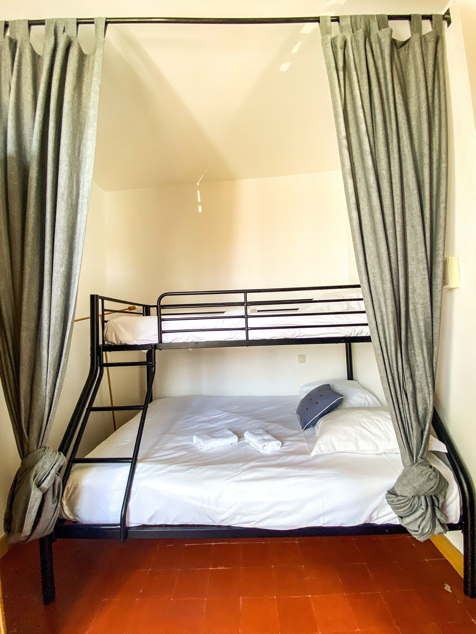 A bunk bed with grey curtains, white bedding, and a single pillow.