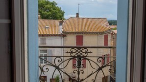 Un balcón con barandilla de hierro forjado, techo de tejas y vistas a edificios con tejados de terracota.