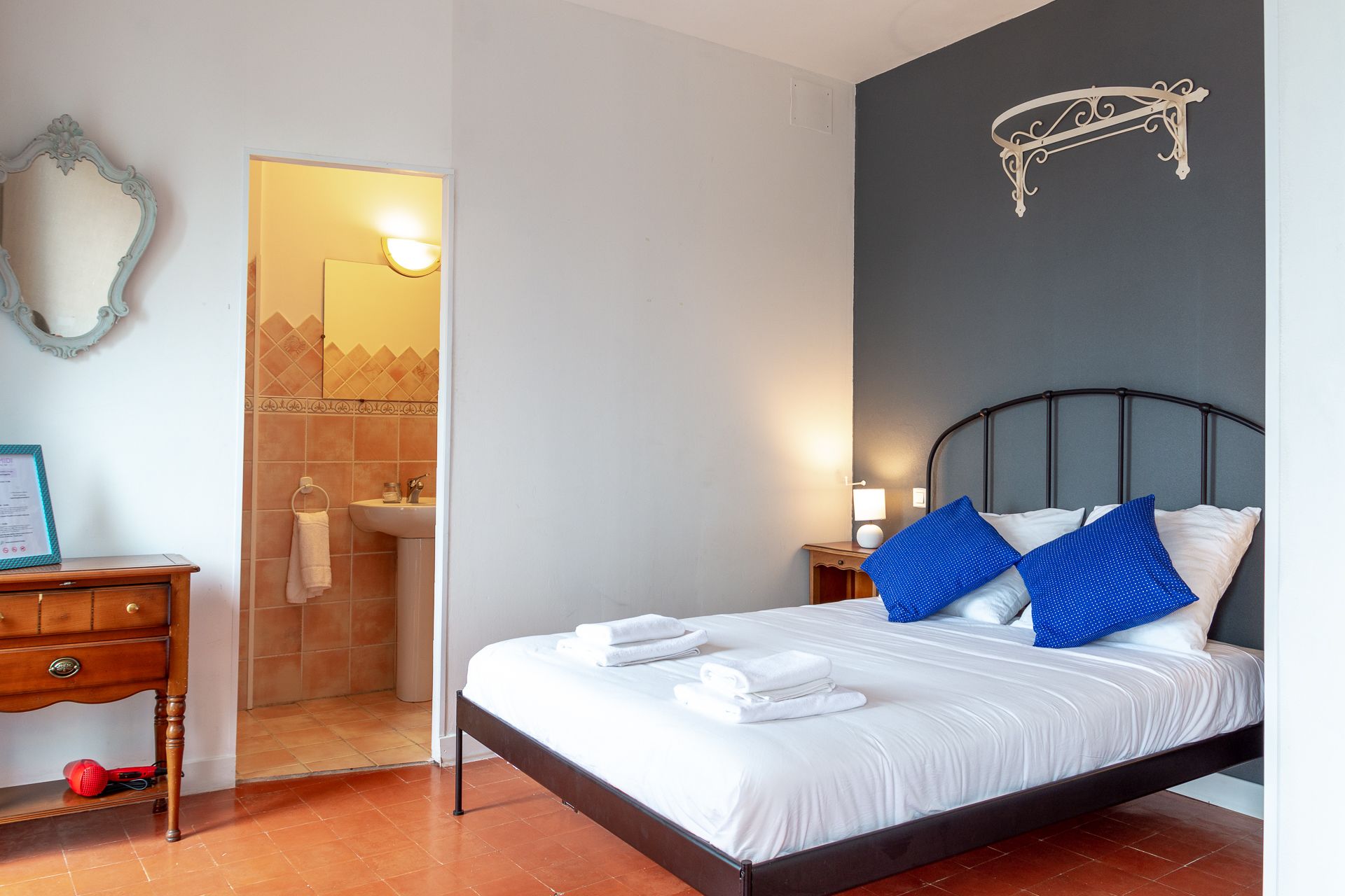 Ein Schlafzimmer mit einem Bett, einem Nachttisch, einem an der Wand montierten Regal und einem durch eine offene Tür einsehbaren Badezimmer.