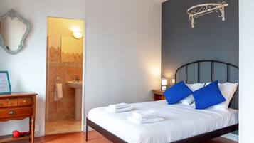Ein Schlafzimmer mit einem Bett, einem Nachttisch, einem an der Wand montierten Regal und einem durch eine offene Tür einsehbaren Badezimmer.